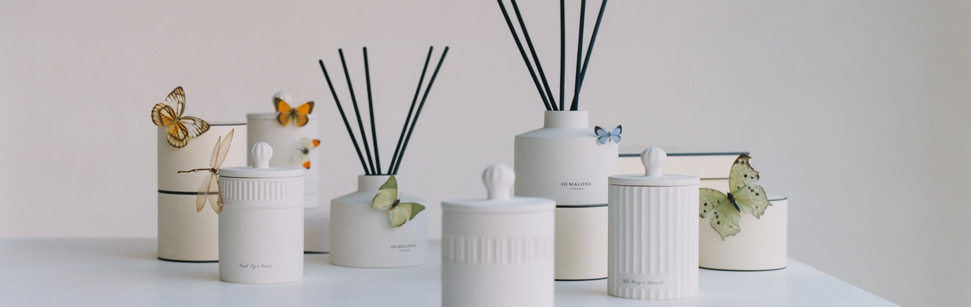image d'une cheminée avec une bougie de voyage, un diffuseur, une bougie et un spray d'ambiance Jo Malone dans une gamme de senteurs, à côté d'un buste